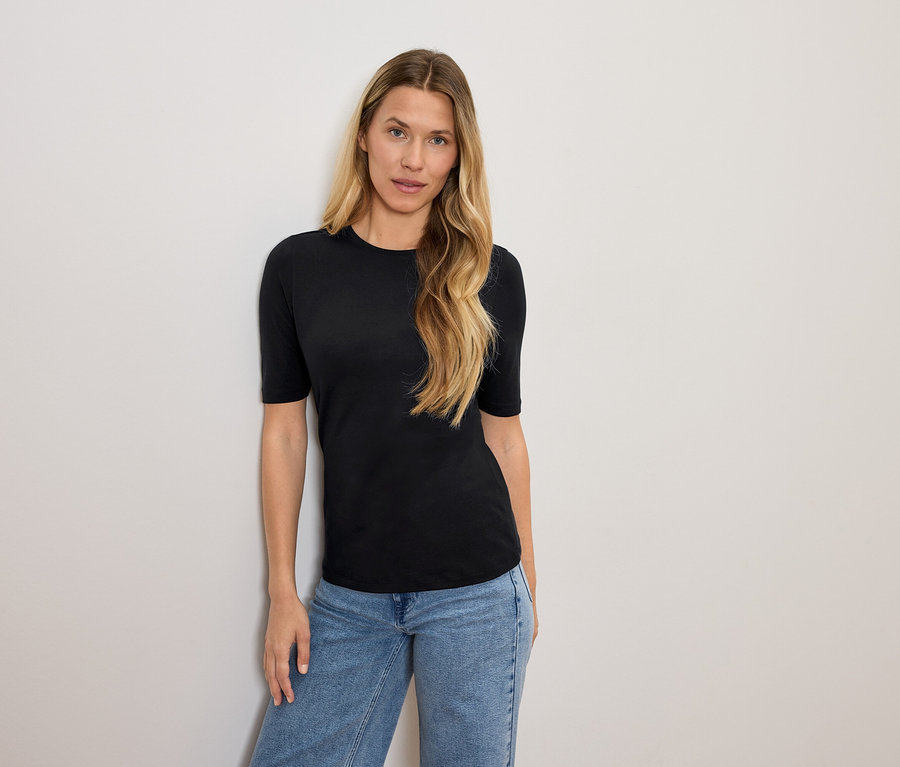 Kobieta o blond włosach pozuje w czarnej koszulce i niebieskich dżinsach.