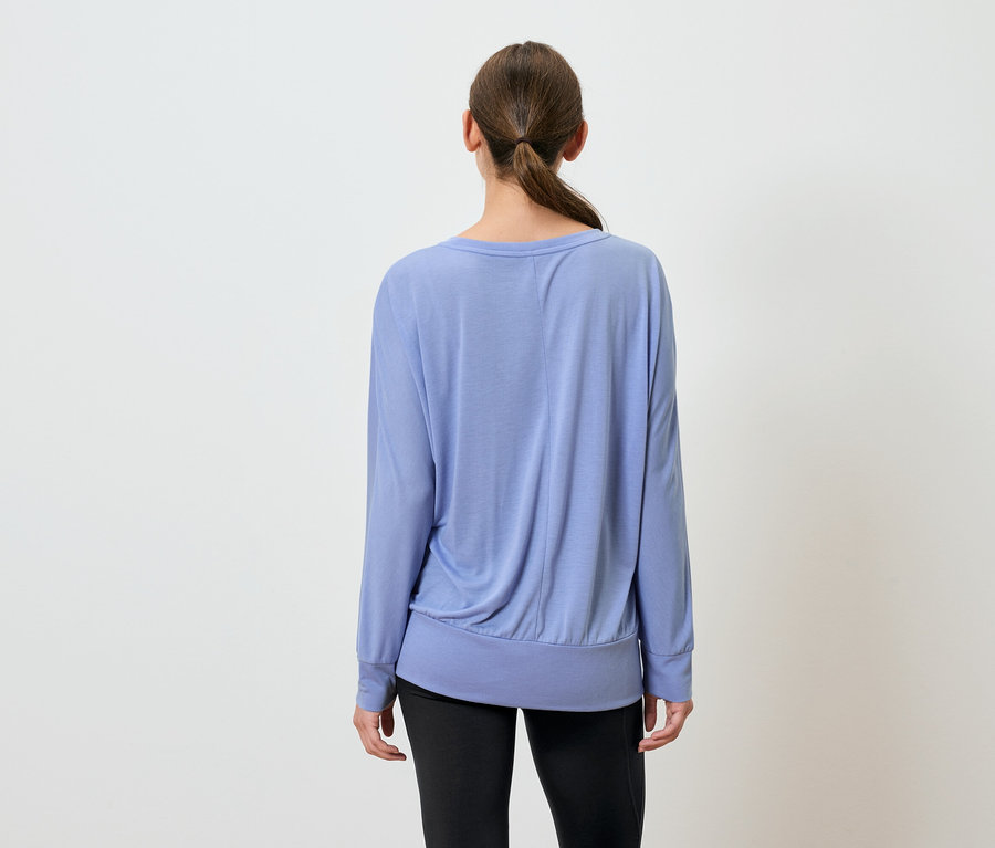 Kobieta tyłem do kamery ma na sobie niebieski top z długim rękawem i czarne spodnie.