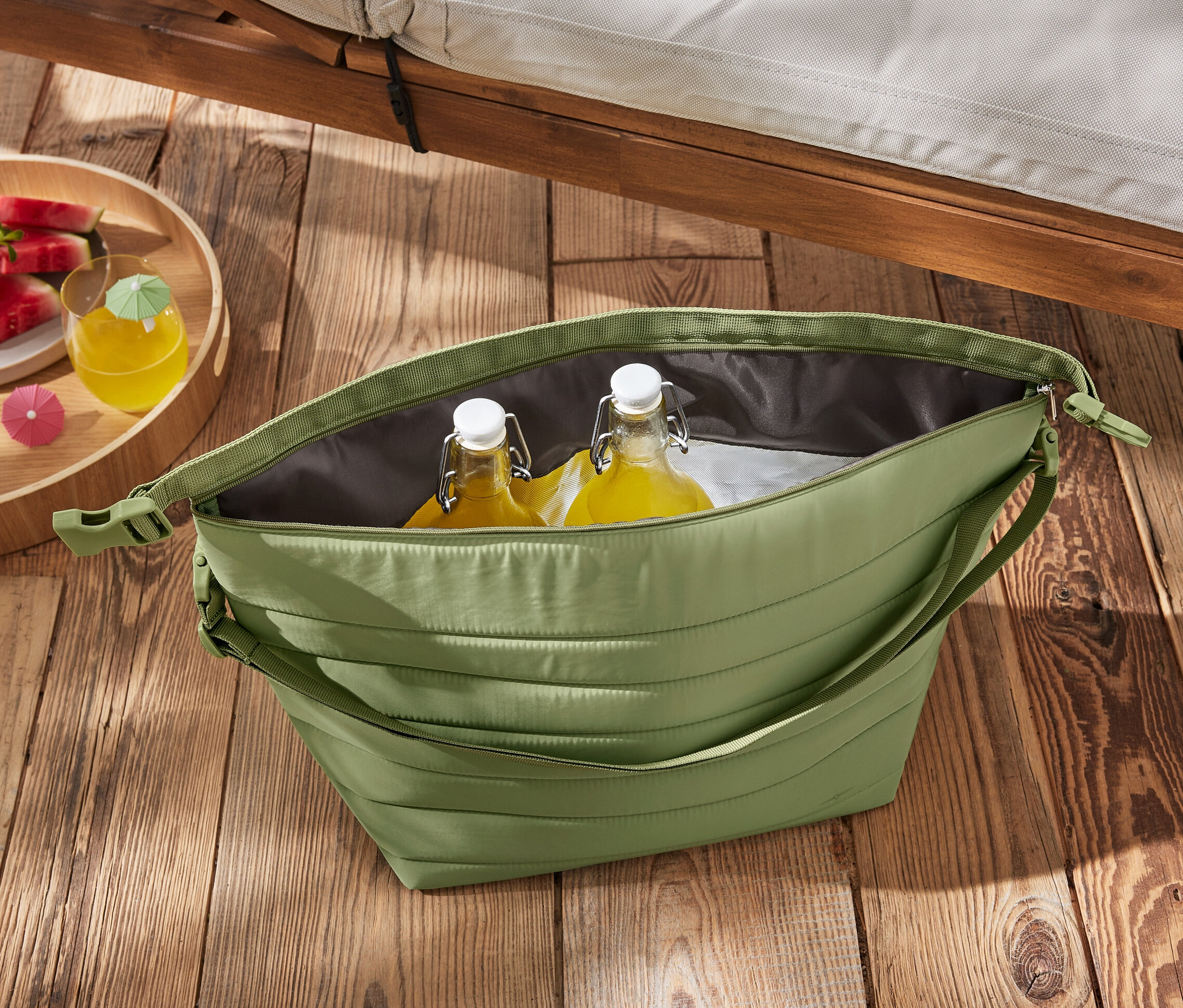 Zielona torba termoizolacyjna z butelkami i arbuzem na drewnianym stole.