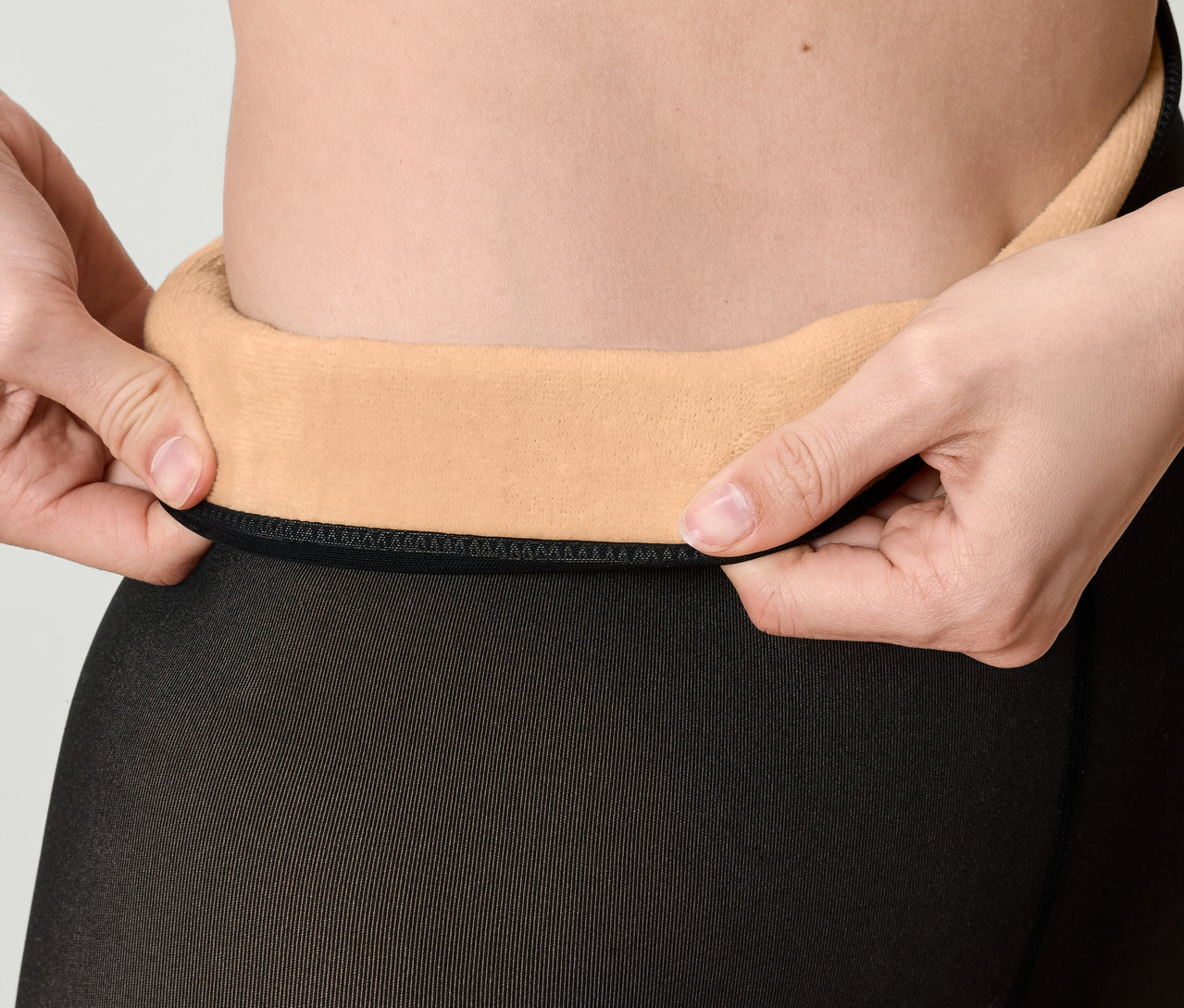 Zbliżenie na kobietę podciągającą pas czarnych rajstop z beżową polarową podszewką.