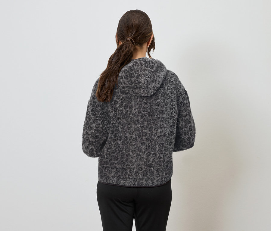 Kobieta tyłem do kamery ma na sobie szarą bluzę z kapturem we wzór zwierzęcy i czarne spodnie.