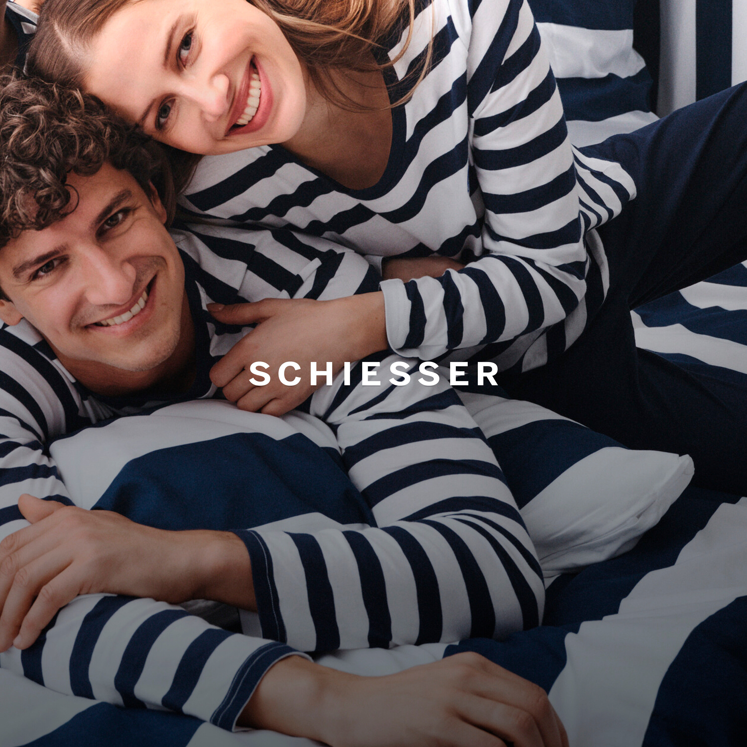 Uśmiechnięta para w piżamach w paski leży na łóżku w pościeli w paski.