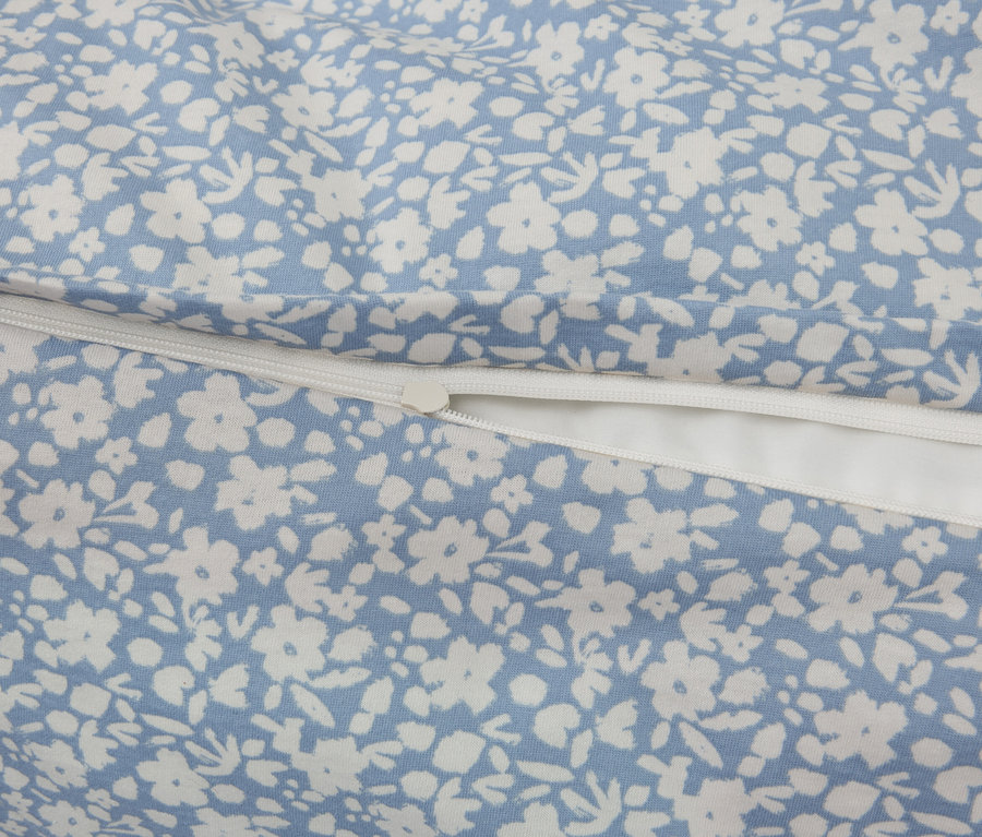 Zbliżenie tkaniny z niebieskim tłem i białym kwiatowym wzorem, uzupełnione białym zamkiem błyskawicznym.