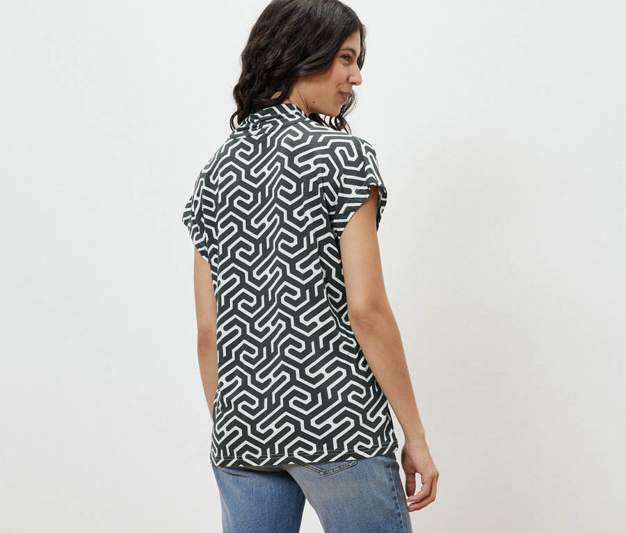 Z profilu kobieta ubrana w zieloną bluzkę z dekoltem w serek i dżinsy.