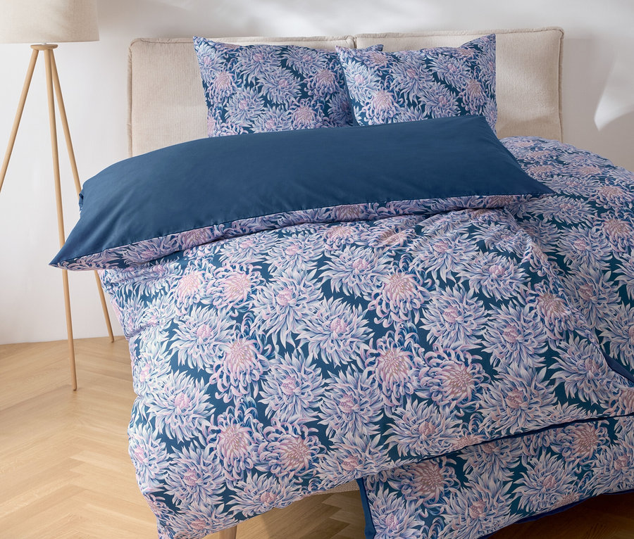 Zbliżenie na łóżko z pościelą w kwiaty i niebieską poduszką.