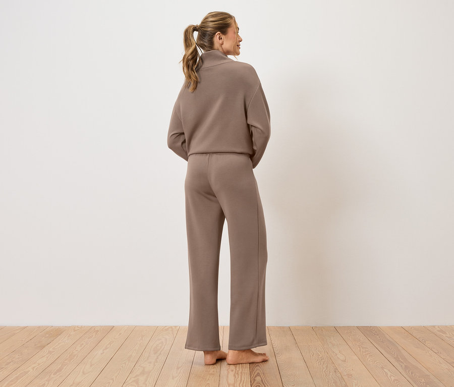 Kobieta stoi tyłem do kamery, ubrana w brązowy garnitur.