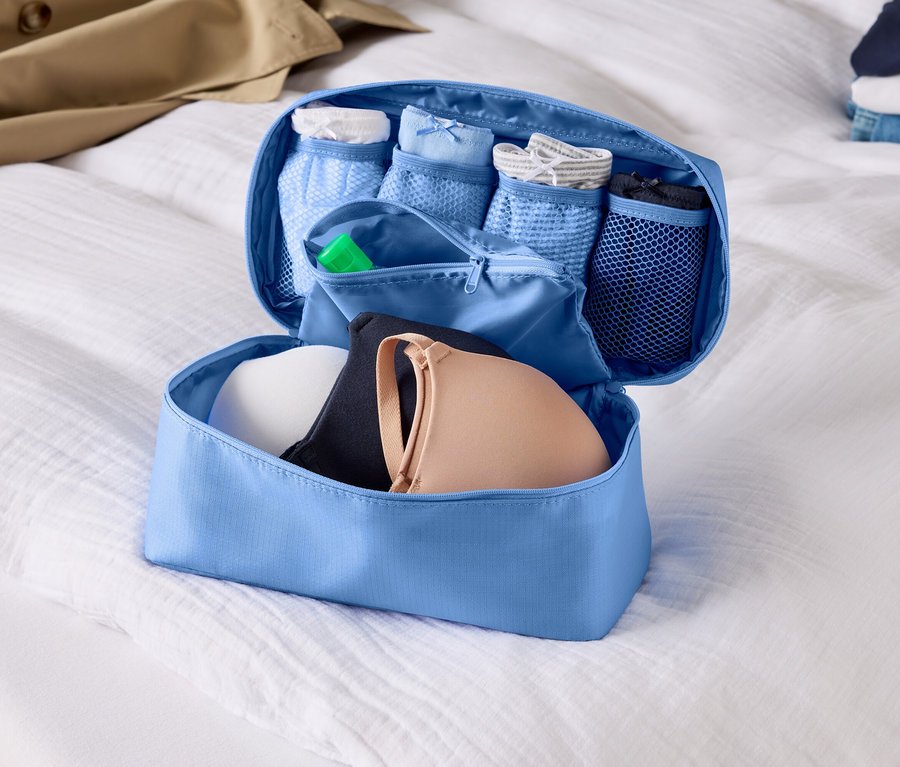 Otwarty, jasnoniebieski organizer bagażowy z biustonoszami i bielizną na białym prześcieradle.