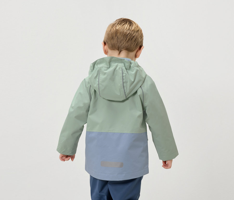 Widok z tyłu dziecka o blond włosach w dwukolorowej kurtce w kolorach zielonym i niebieskim.