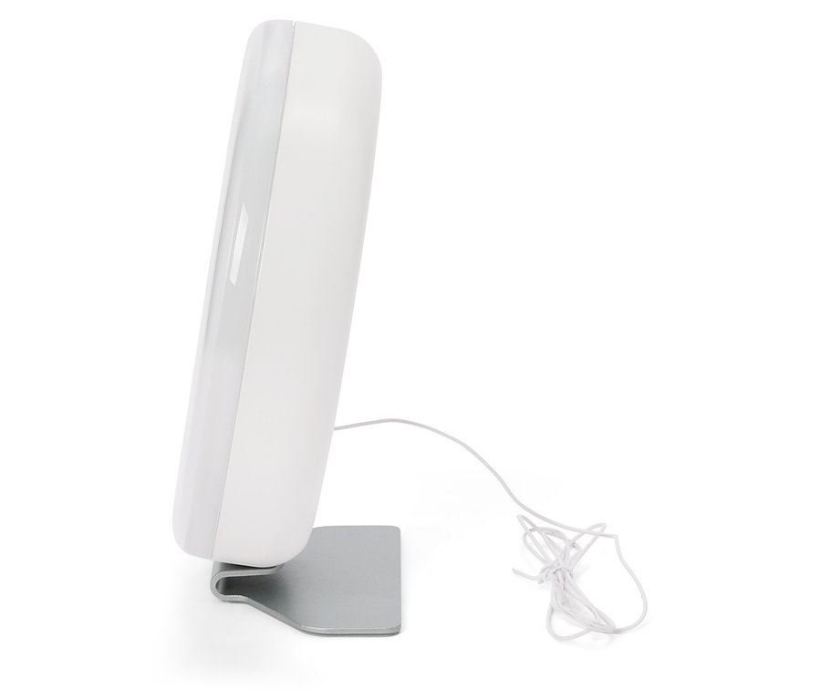 Biała lampa do światłoterapii stoi na srebrnej podstawce, obok leży kabel.