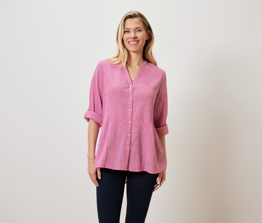 Kobieta o blond włosach ma na sobie różową bluzkę i ciemne spodnie.