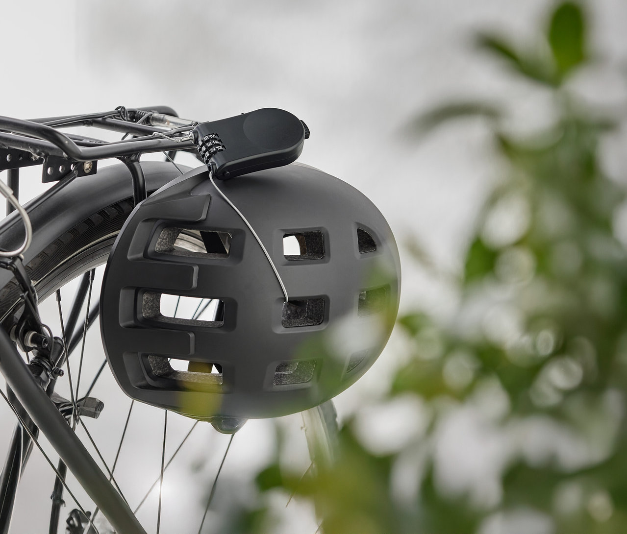 Czarny kask rowerowy z zamkiem szyfrowym wisi na bagażniku rowerowym.