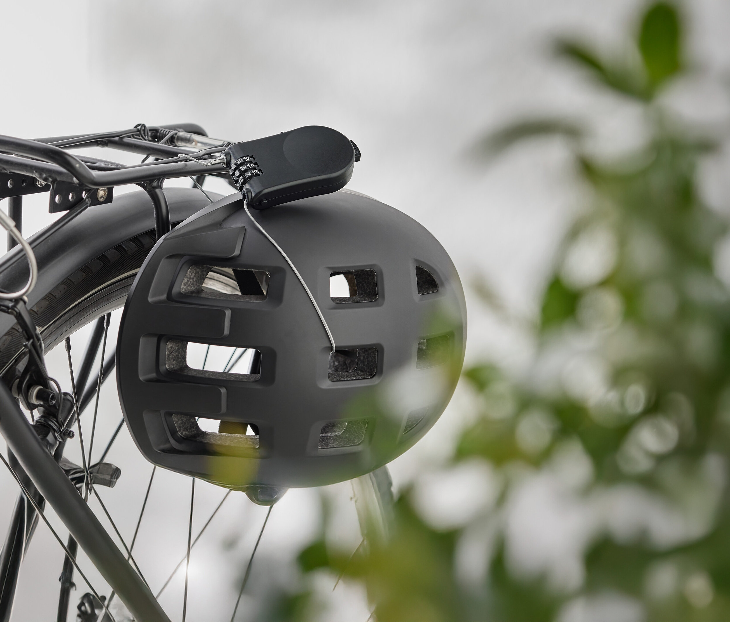 Czarny kask rowerowy z zamkiem szyfrowym wisi na bagażniku rowerowym.