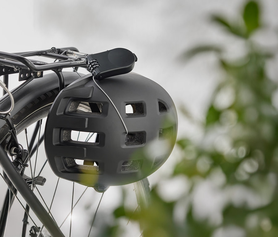 Czarny kask rowerowy z zamkiem szyfrowym wisi na bagażniku rowerowym.