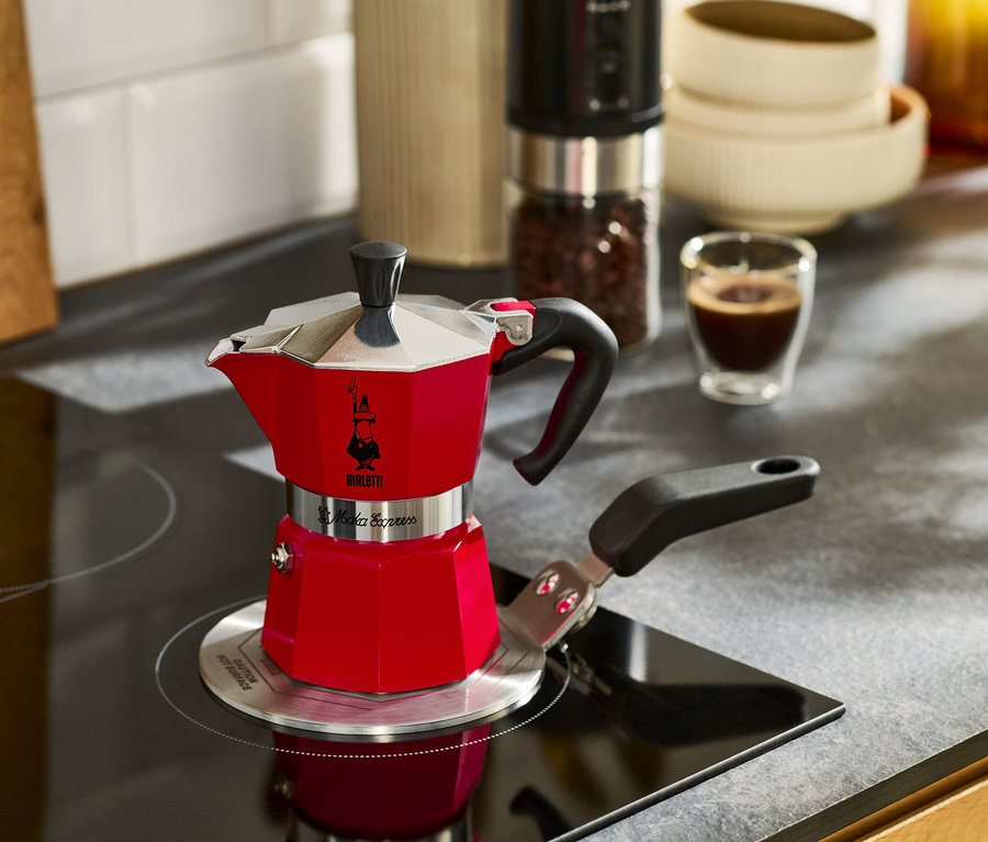 Czerwony ekspres do kawy stoi na płycie kuchennej obok filiżanki espresso.
