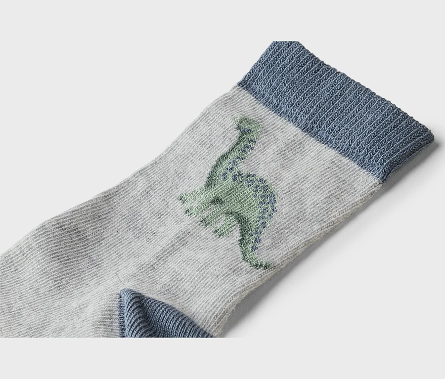 Zbliżenie szarej skarpetki z niebieskim ściągaczem i zielonym motywem dinozaura.