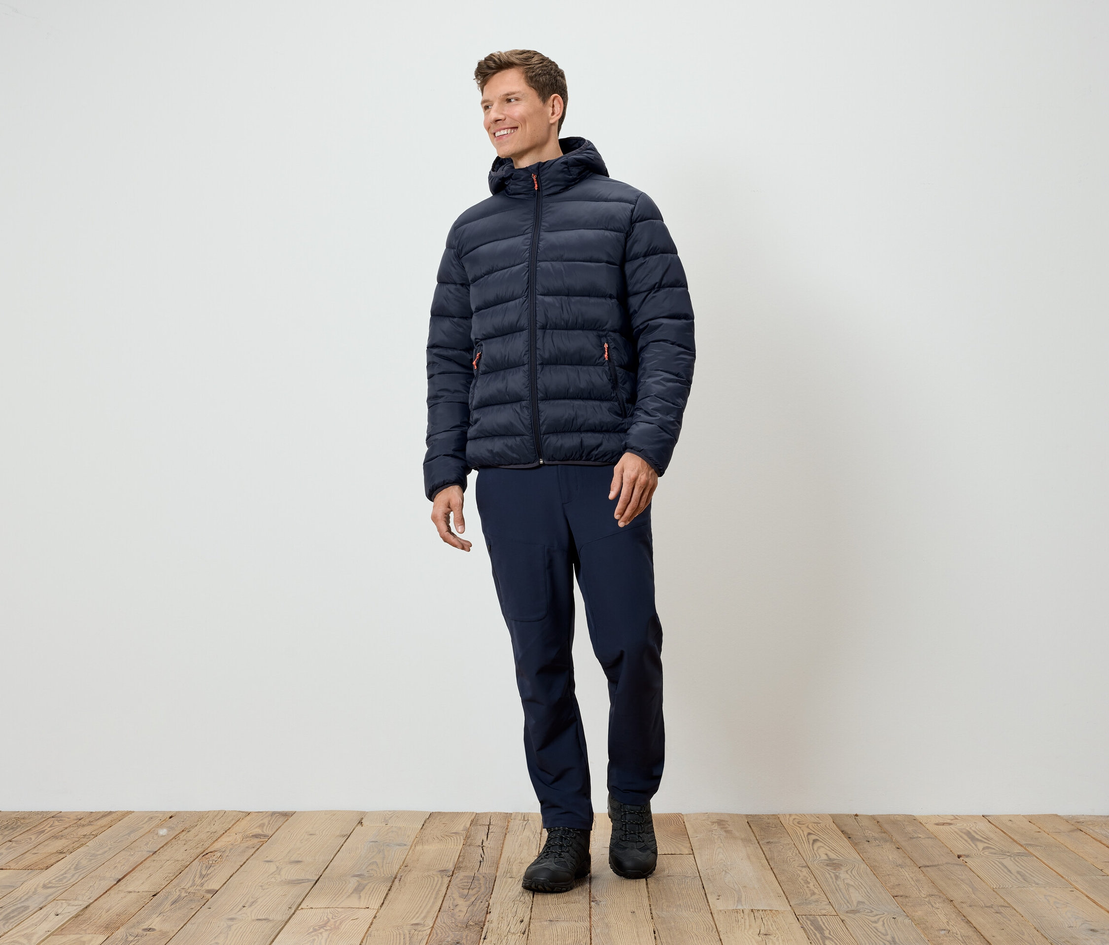 Mężczyzna stoi w ciemnoniebieskiej kurtce puchowej, granatowych spodniach i czarnych butach.