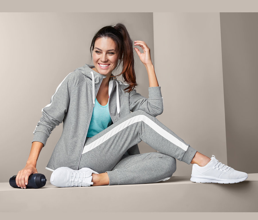 Kobieta siedzi w szarych damskich bawełnianych spodniach dresowych i białych tenisówkach.