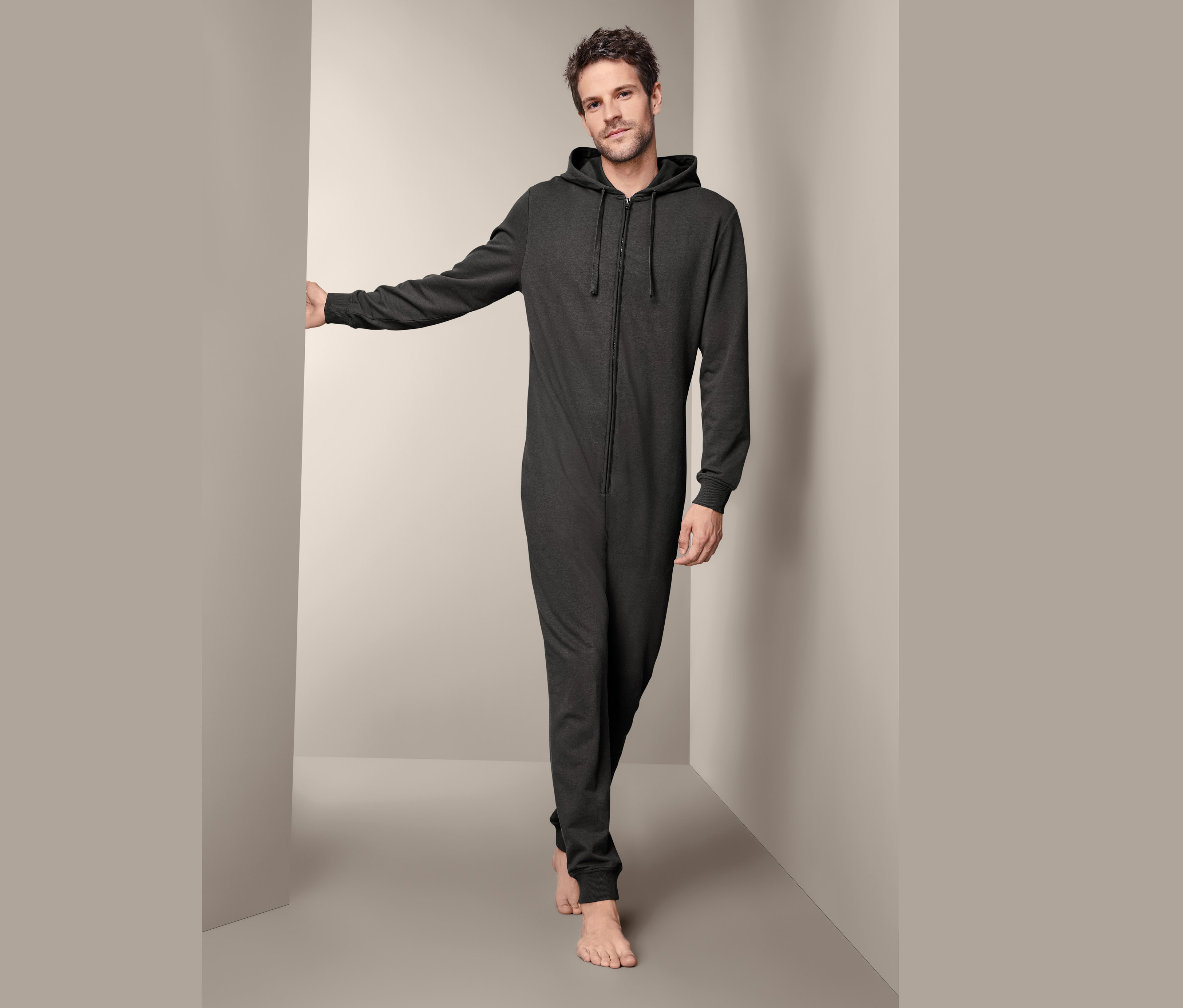 Mężczyzna w męskim kombinezonie rekreacyjnym z kapturem i zamkiem błyskawicznym stoi w rogu pokoju.