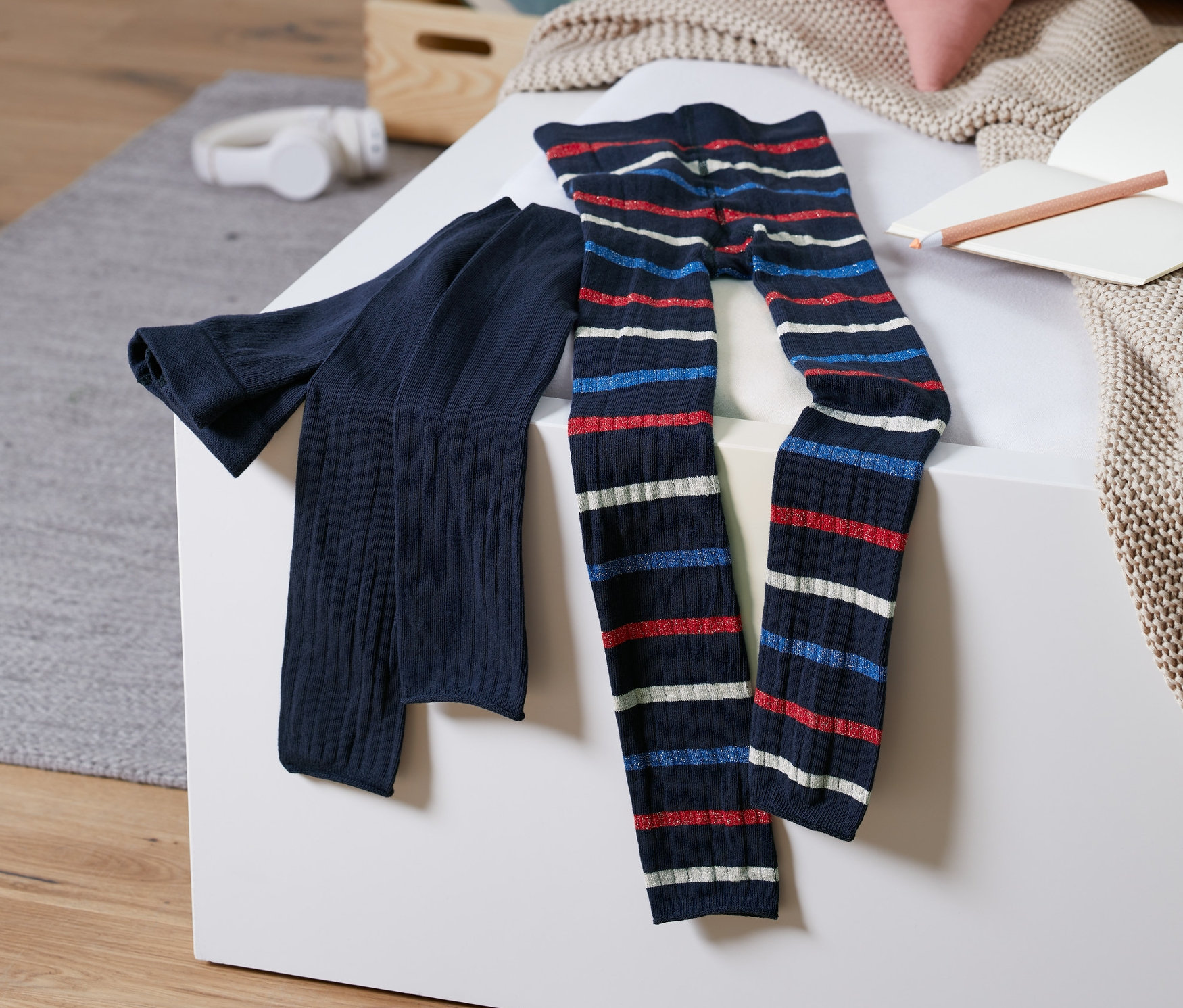 Dwie pary legginsów z dzianiny leżą na białej powierzchni. Jedne są granatowe, a drugie mają czerwono-biało-niebieskie poziome paski.