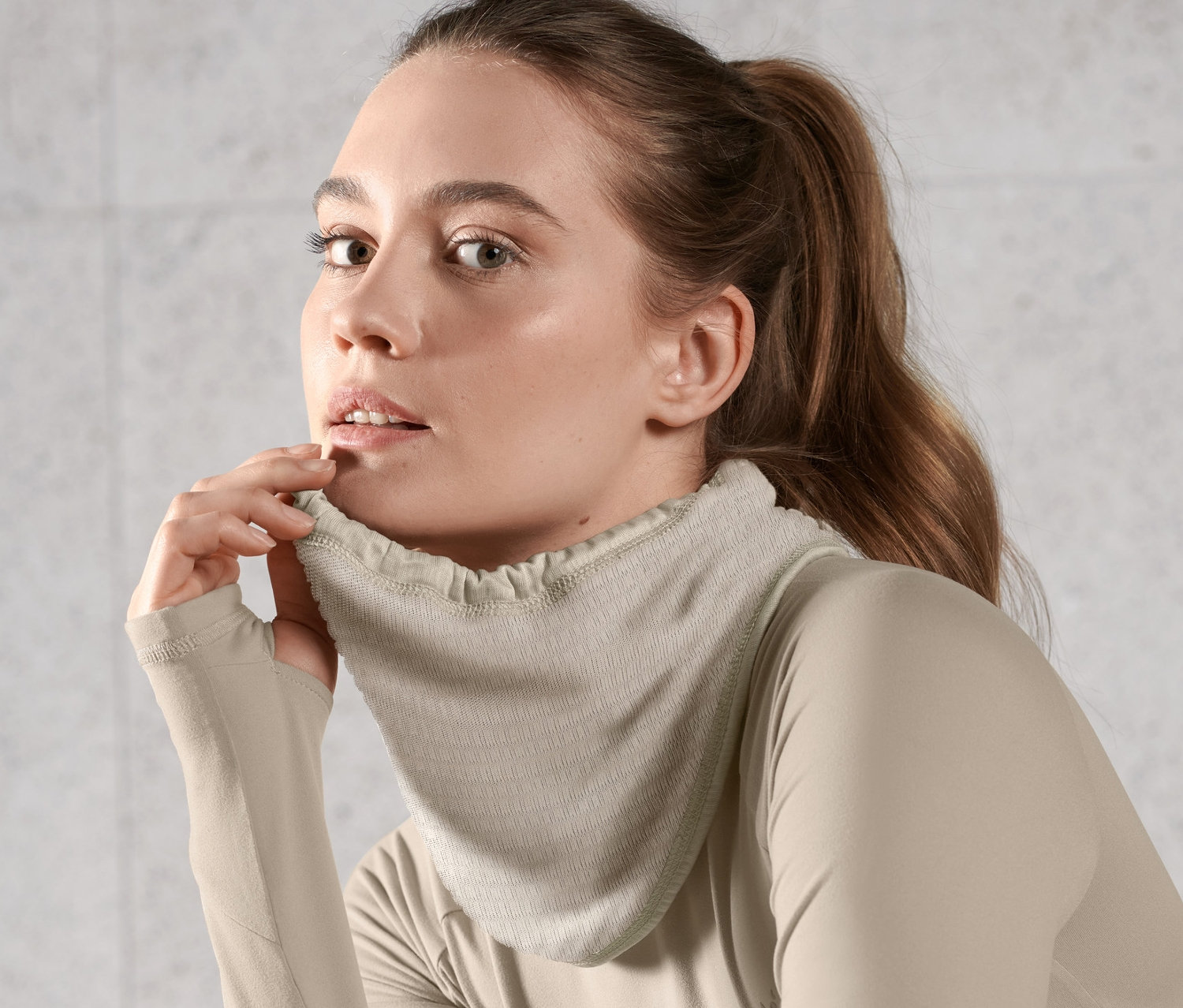 Kobieta nosi jasnobrązową chustę wielofunkcyjną i bluzkę z długim rękawem.