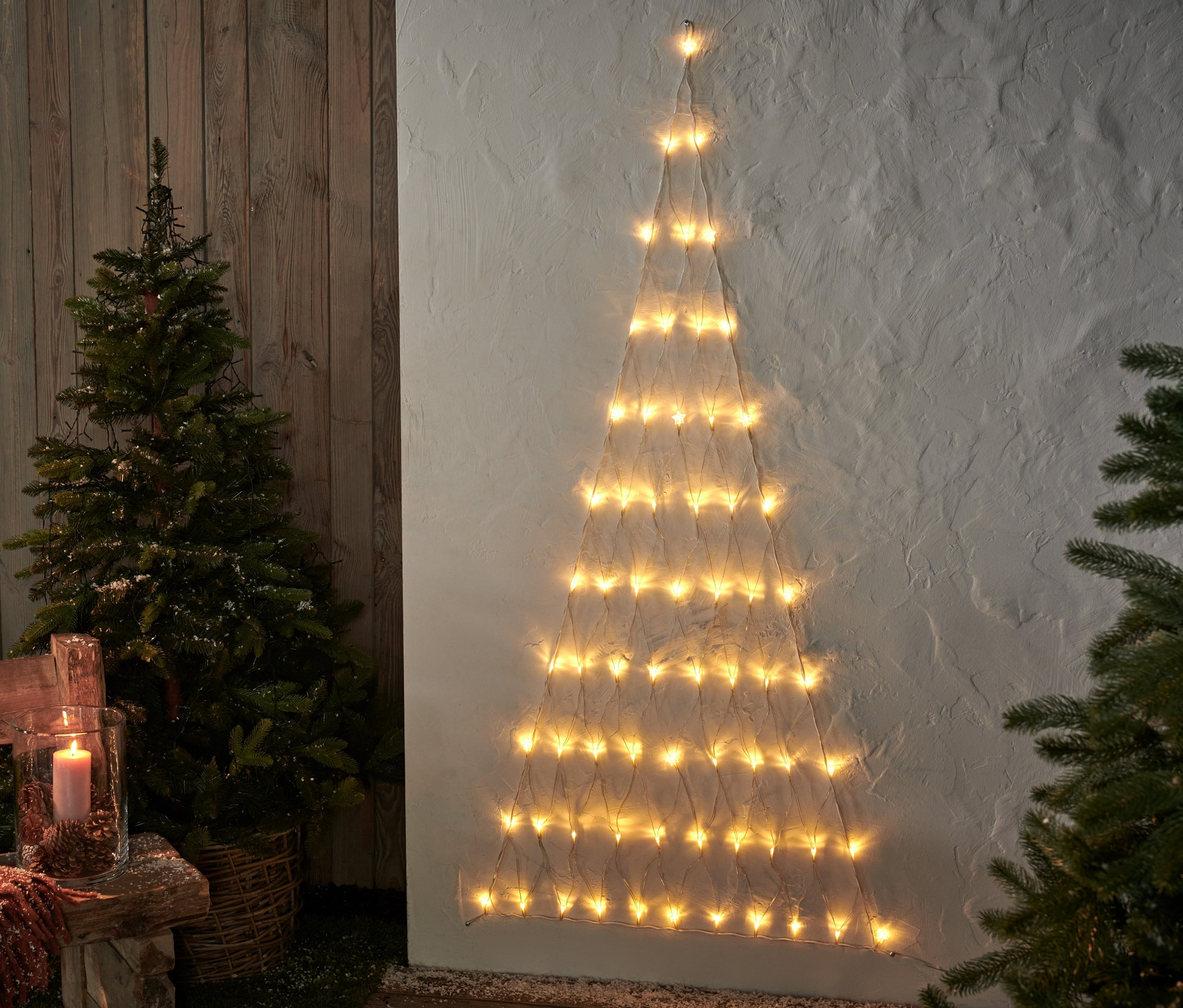 Podświetlana dekoracja LED Choinka wisi na ścianie obok małego drzewka.