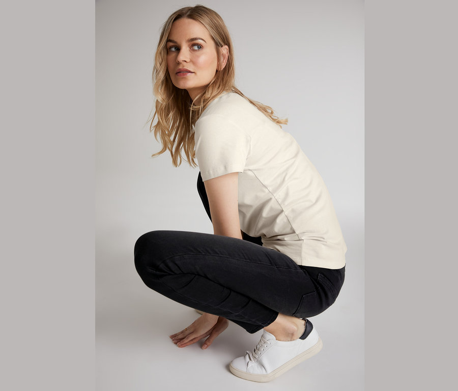 Kobieta w kucki ma na sobie dżinsowe spodnie skinny, t-shirt i trampki.