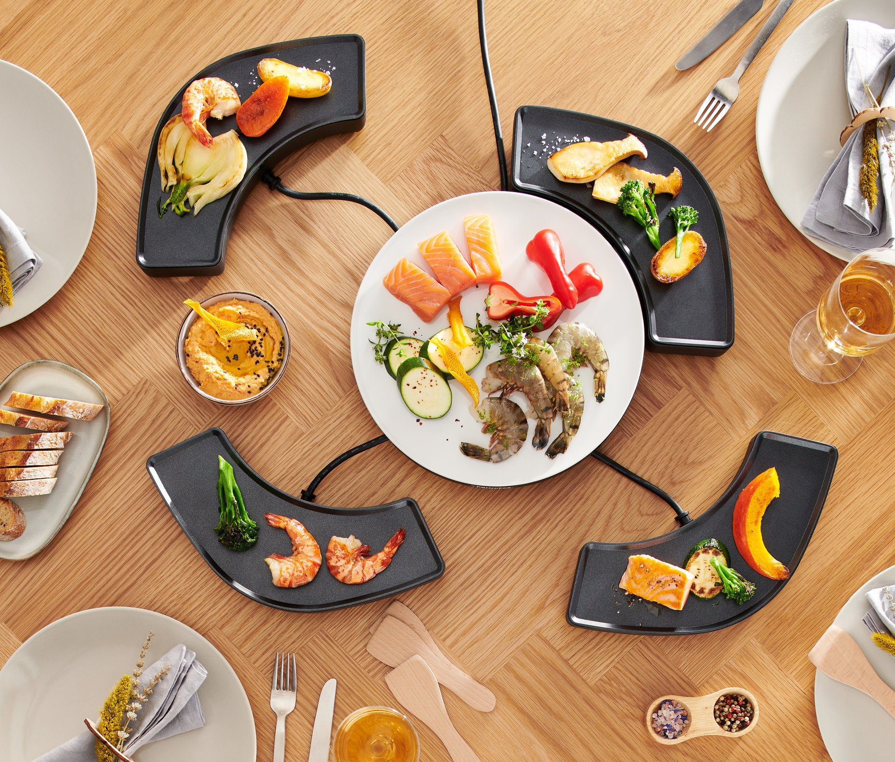 Widok z góry na stół z grillem stołowym „Dinner4All”, talerzami, jedzeniem i napojami.