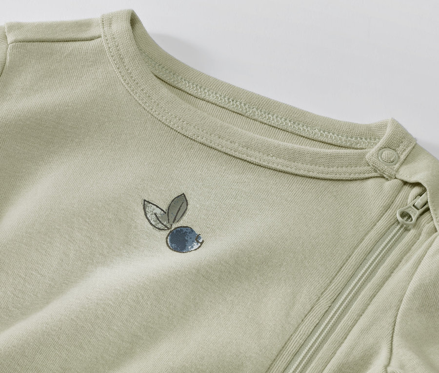 Zbliżenie na jasnozieloną piżamę dziecięcą z nadrukiem jagód i zamkiem błyskawicznym.