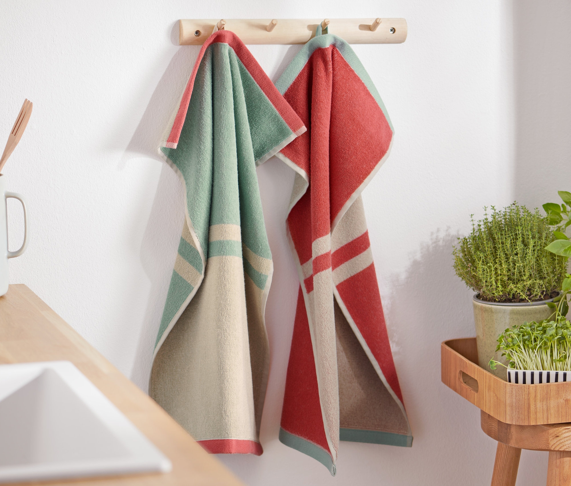 Dwa ręczniki kuchenne wiszą na drewnianym wieszaku.