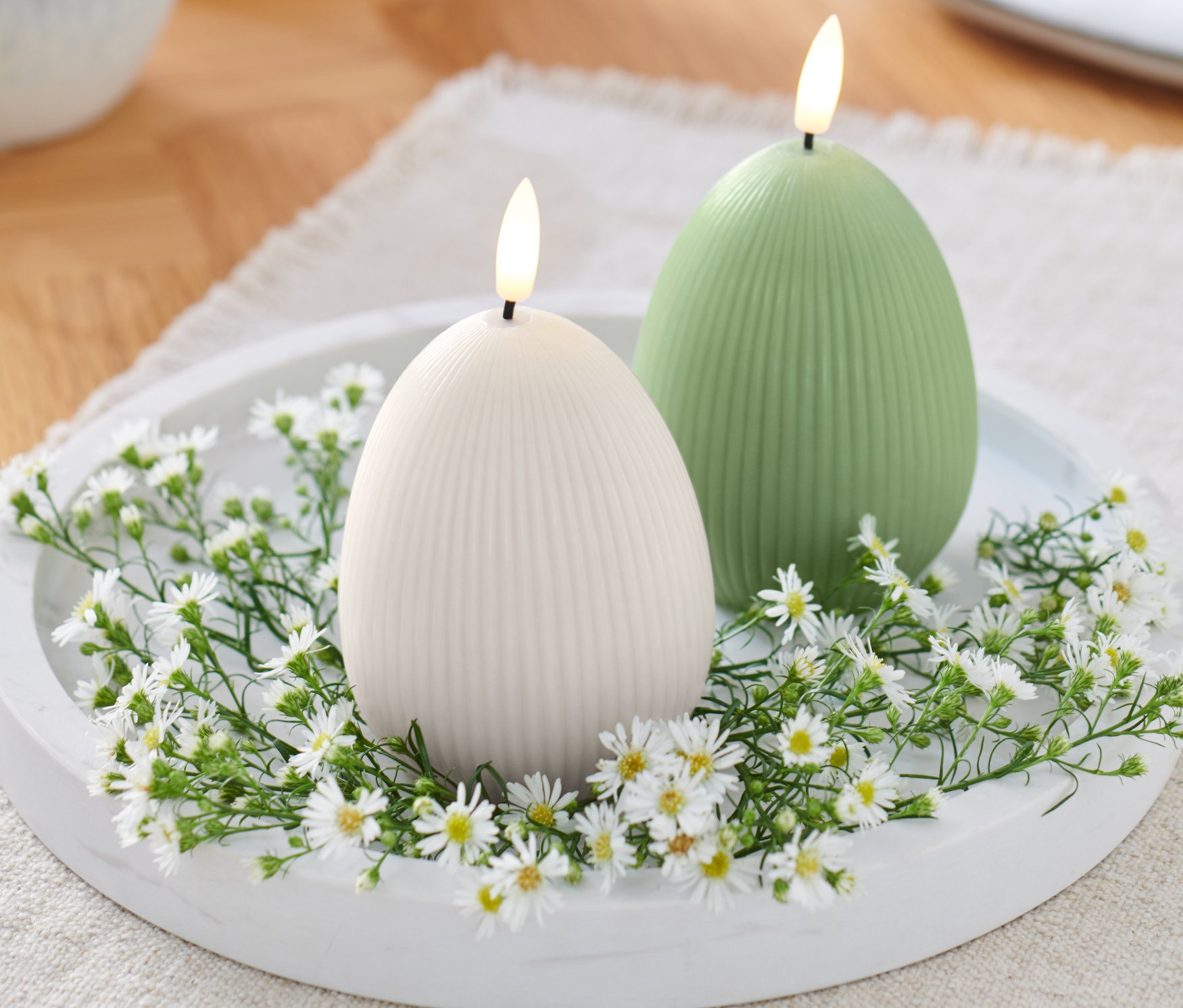Dwie świece LED z prawdziwego wosku na białym talerzu, otoczone białymi kwiatami.
