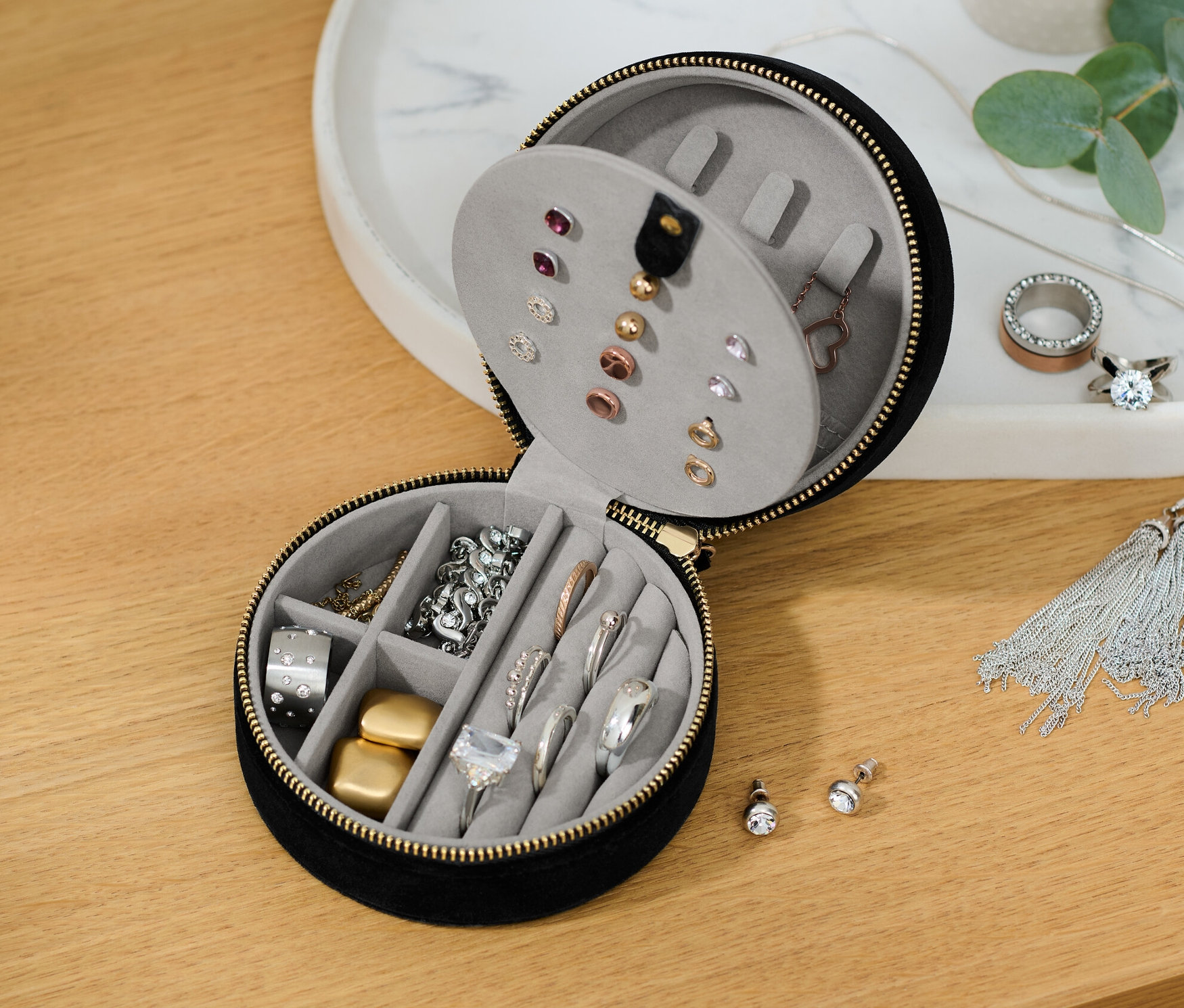 Częściowo otwarta mała kasetka na biżuterię z różnymi elementami biżuterii w środku.