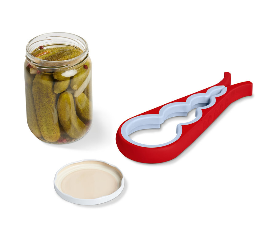 Słoik z ogórkami, pokrywka i czerwony otwieracz do słoików i butelek leżą obok siebie.