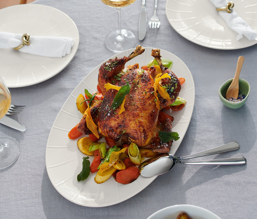 Pieczony kurczak na paterze do serwowania z dodatkami na stole.