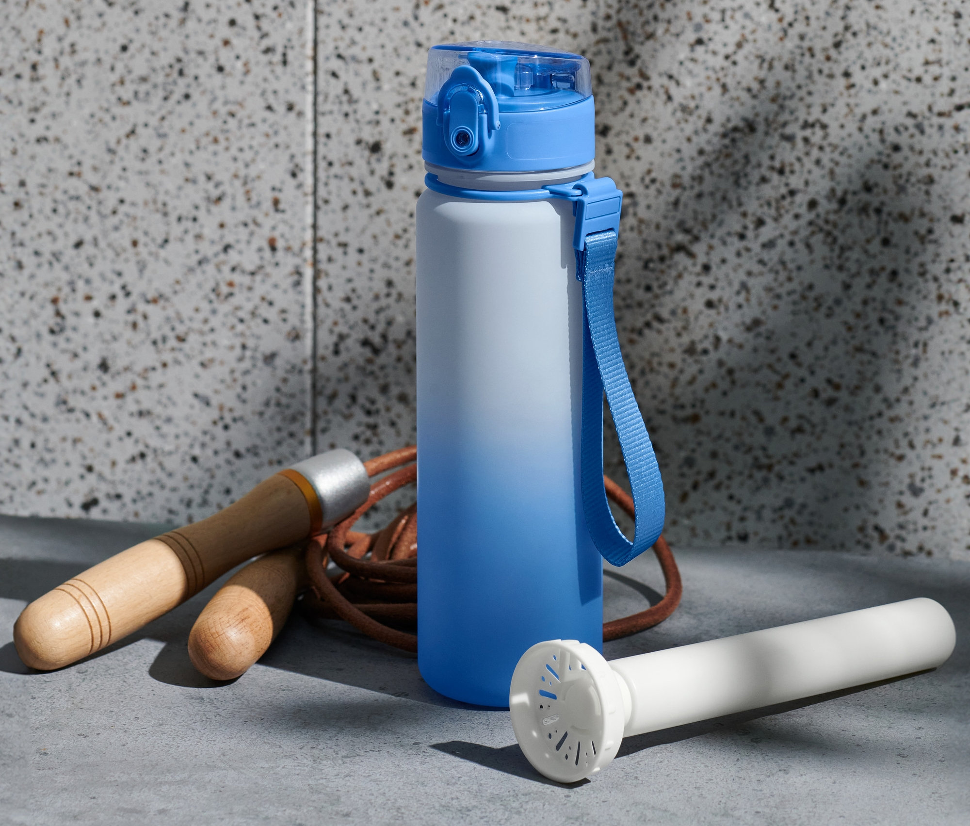 Niebiesko-biały bidon stoi obok skakanki i białego cylindra chłodzącego.