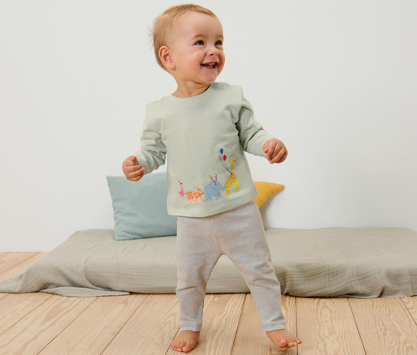 Uśmiechnięte dziecko stoi i ma na sobie 2 koszulki z długim rękawem z motywem zwierzęcym.