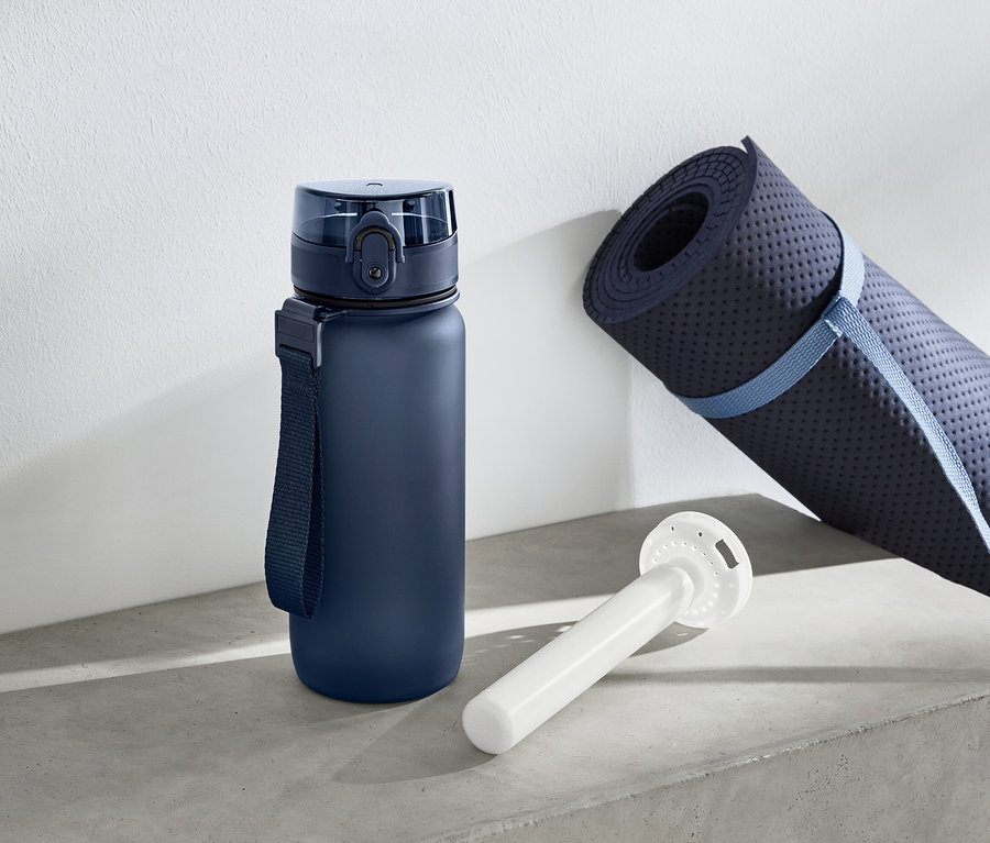 Niebieska butelka na wodę stoi obok zwiniętej maty do ćwiczeń i białego cylindrycznego przedmiotu.