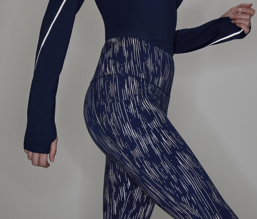 Częściowy widok kobiety w granatowej bluzce z długim rękawem i wzorzystych legginsach.