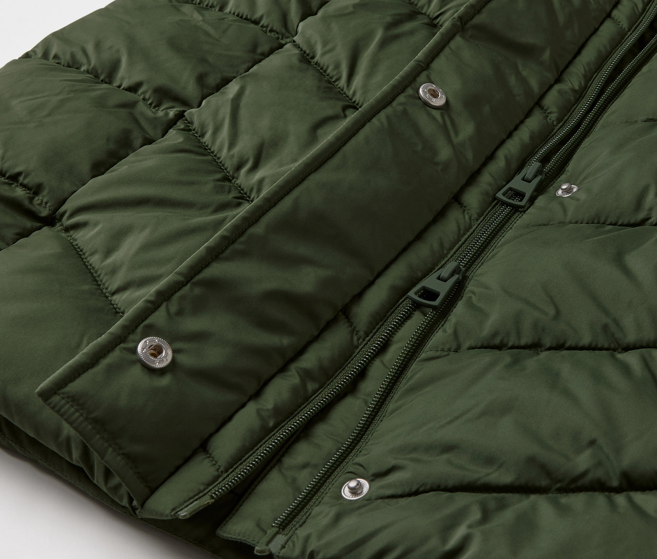 Szczegółowe ujęcie ciemnozielonej kurtki puchowej z kapturem.