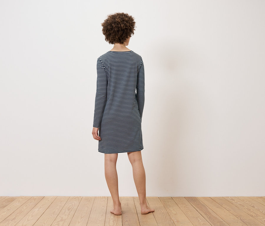 Kobieta stoi tyłem do kamery, ubrana w sukienkę w paski.