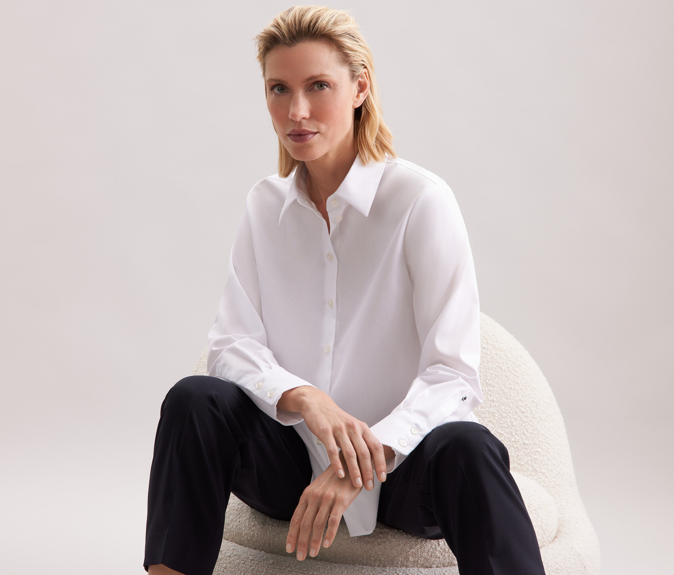 Kobieta siedzi na krześle w białej koszuli i czarnych spodniach.