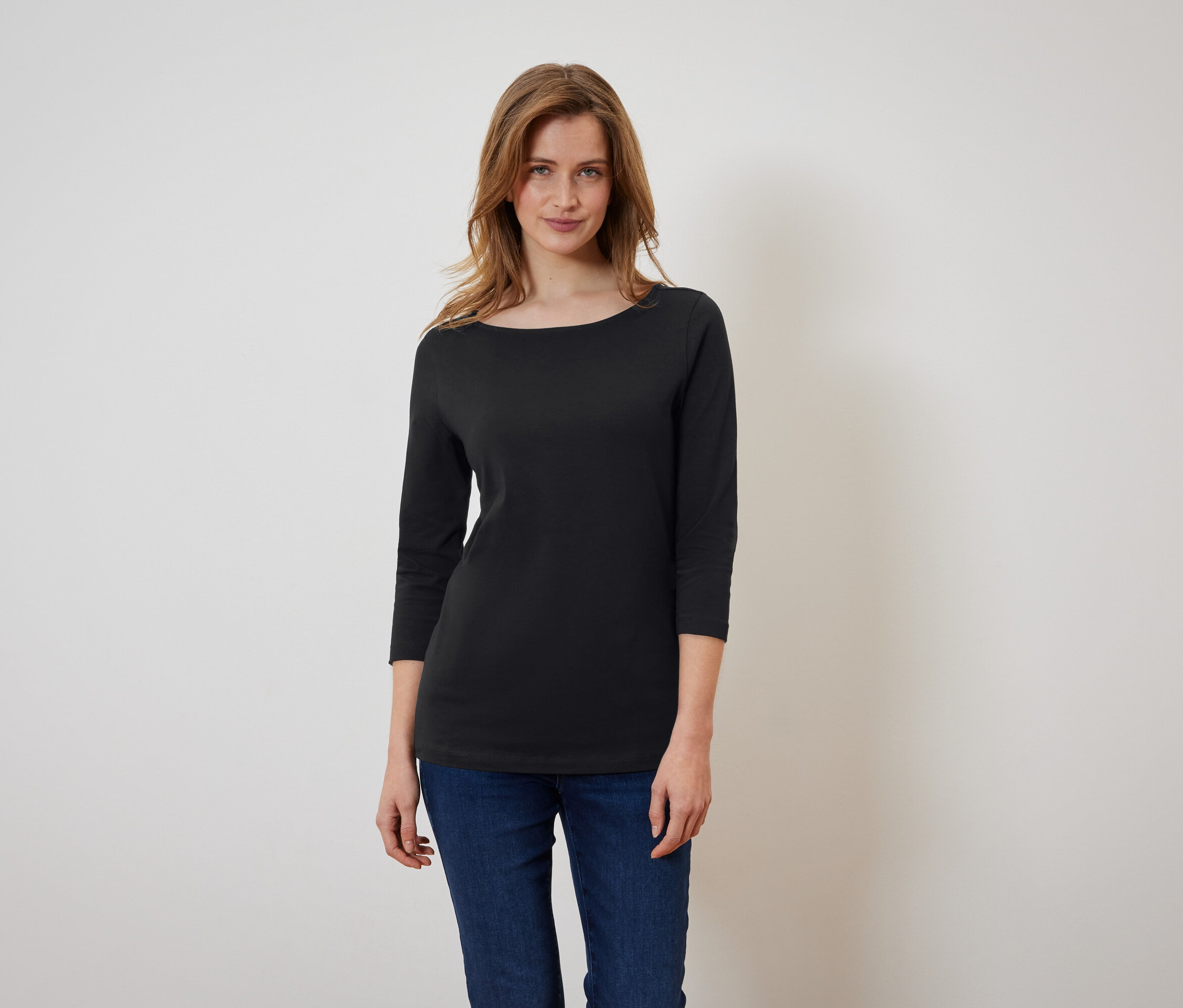 Kobieta ma na sobie czarną koszulkę z rękawami trzy czwarte i niebieskie dżinsy.