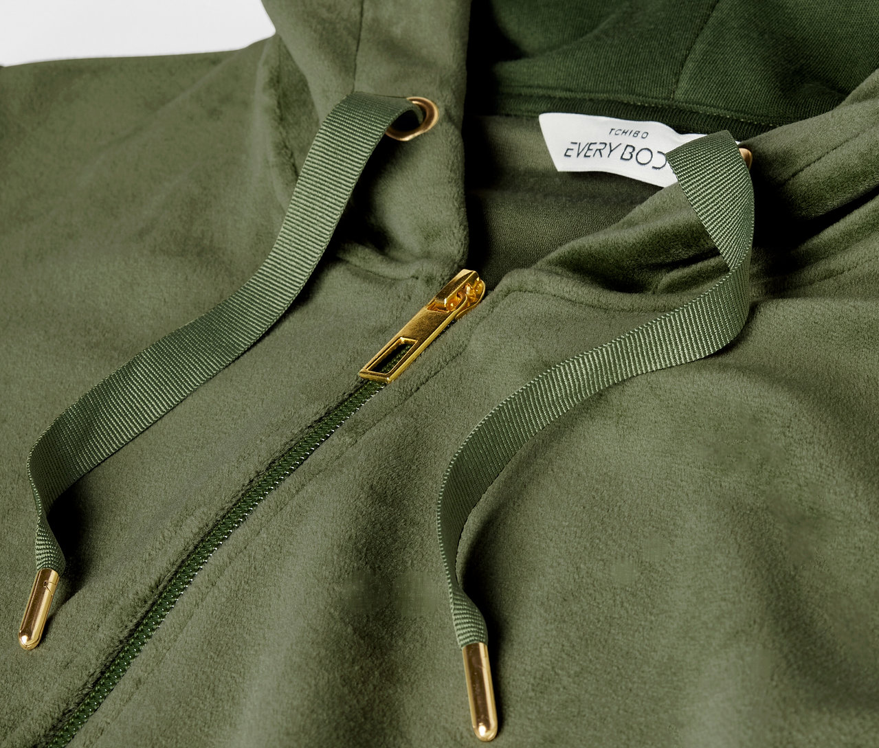 Szczegół zielonej bluzy z kapturem z złotym zamkiem błyskawicznym i sznurkiem.