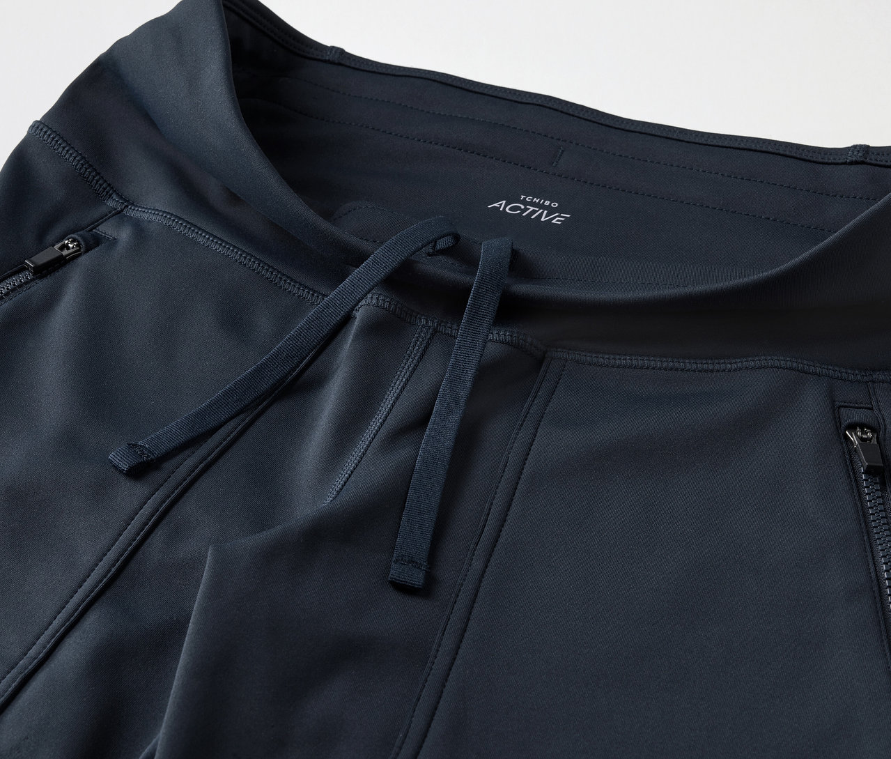 Zbliżenie na granatowe spodnie dresowe z kieszeniami na zamek błyskawiczny i sznurkiem.