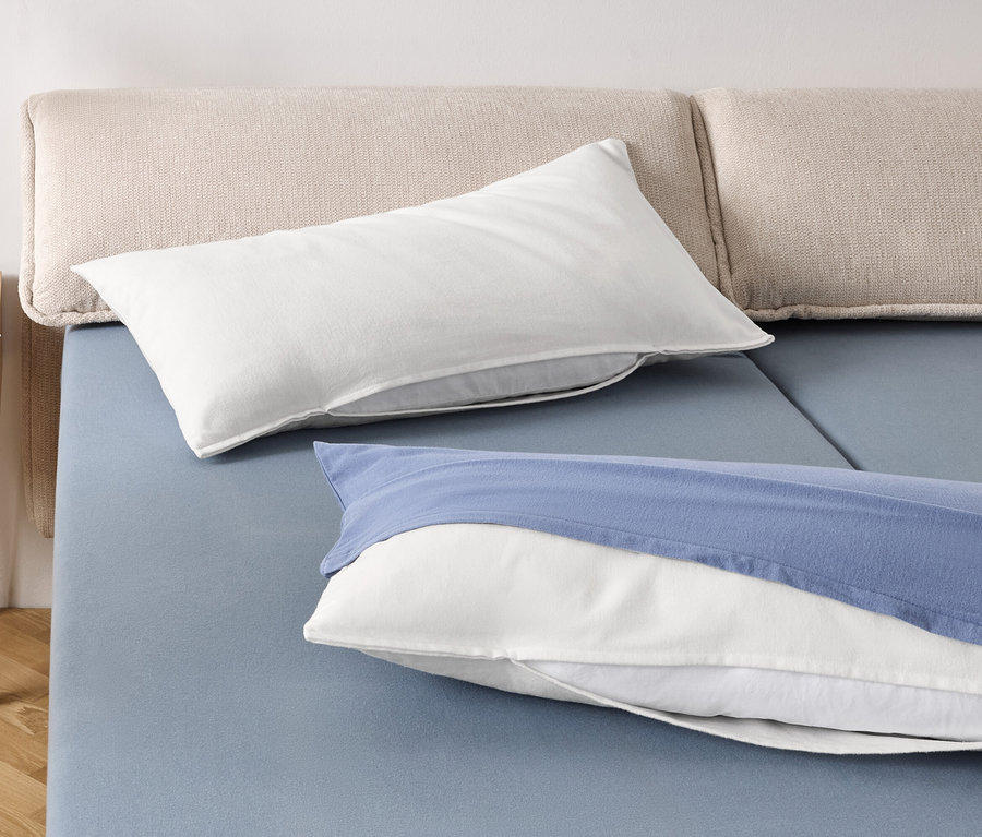 Dwie białe poduszki i jedna biała poduszka z niebieską poszewką na niebieskim łóżku.