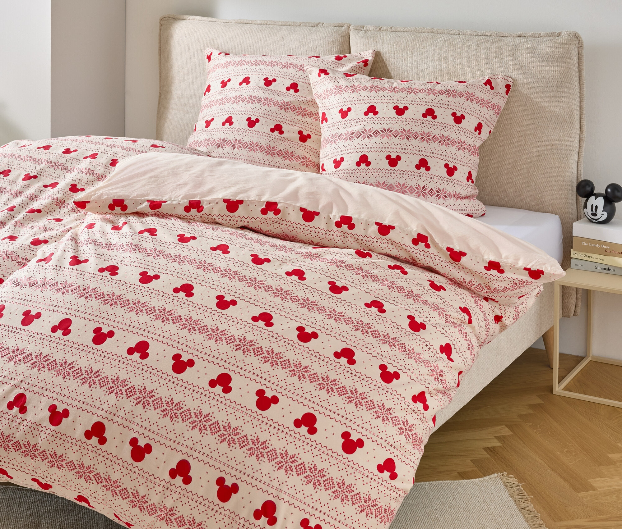 Łóżko z pościelą w motywy Myszki Miki i dwiema poduszkami z podobnym wzorem.