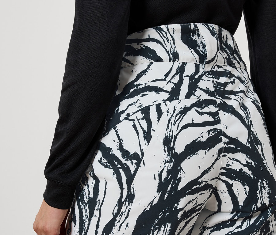 Widok z tyłu kobiety w czarnym topie i białych spodniach we wzór czarnych gałęzi.