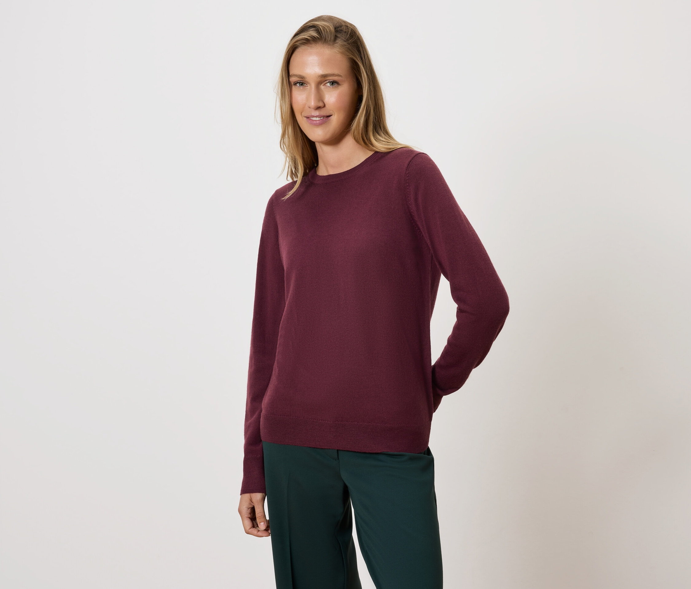 Kobieta pozuje w bordowym swetrze i zielonych spodniach.