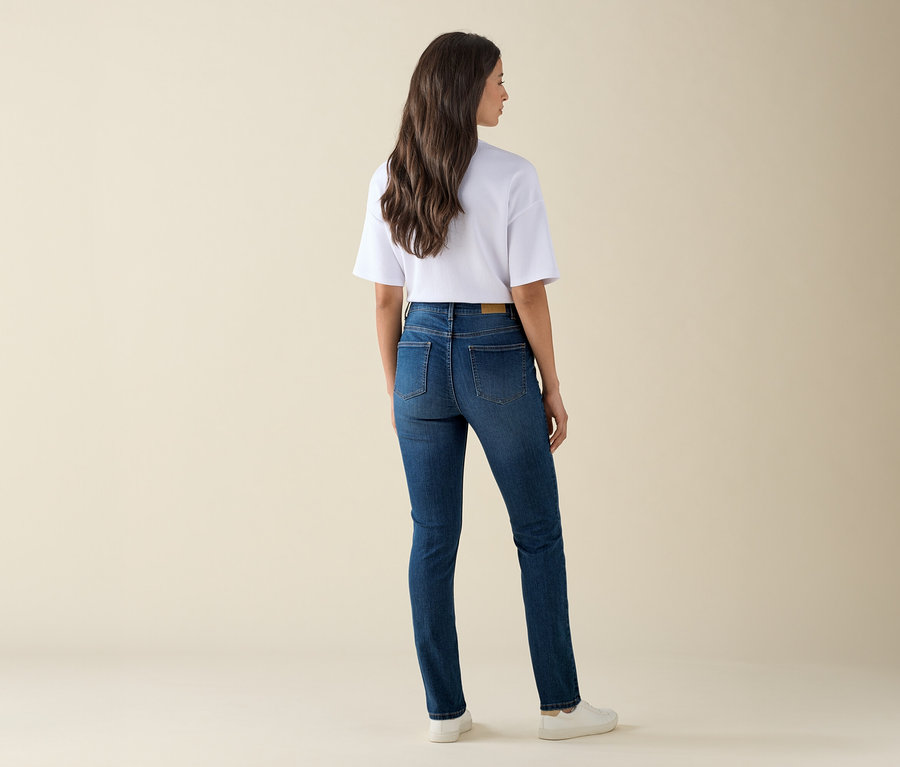 Kobieta stoi tyłem do kamery i ma na sobie dżinsy Slim-Jeans – Fit »Emma«, mid blue denim, biały T-shirt i trampki.