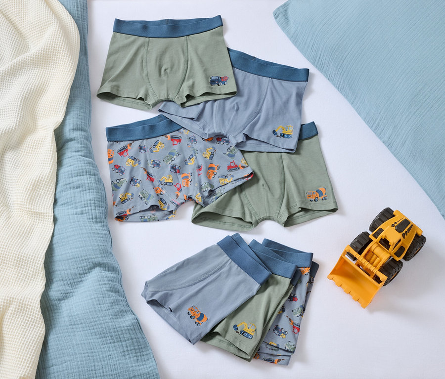 Na łóżku leży sterta chłopięcych bokserek z motywami samochodów i żółta zabawka spychacz.