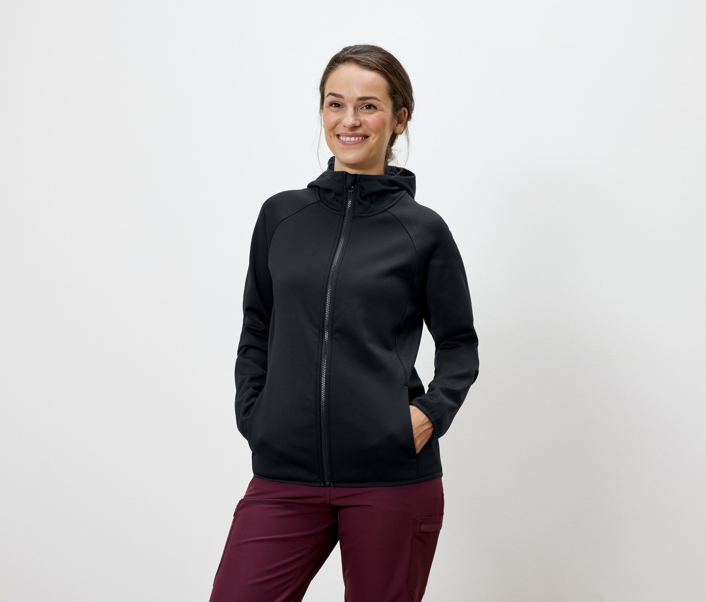 Kobieta pozuje w czarnej bluzie z kapturem i bordowych spodniach.